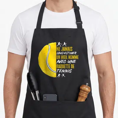 Tablier de cuisine noir avec demi-ballon de tennis jaune et texte humoristique sur le sport.