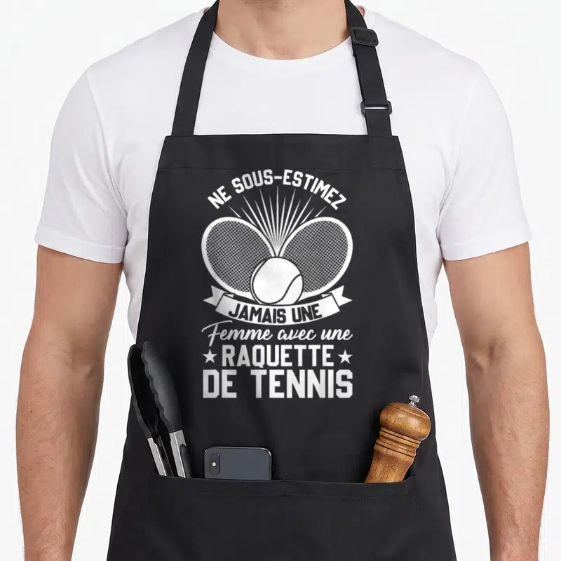 Tablier de cuisine noir avec deux raquettes de tennis croisées et un ballon au centre.