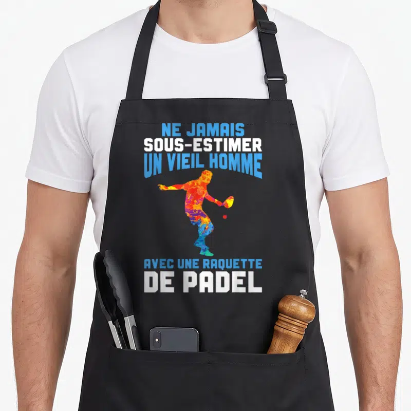 Tablier de cuisine noir avec silhouette multicolore d'un joueur de padel et texte blanc et bleu sur fond uni.