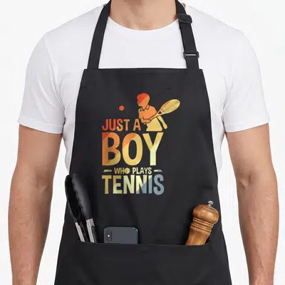 Tablier de cuisine noir avec illustration d'un joueur de tennis et le texte Just a Boy Who Plays Tennis en dégradé orange et jaune.