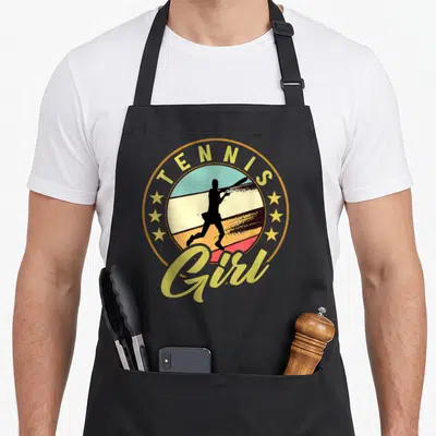 Tablier de cuisine noir avec un logo circulaire vintage représentant une silhouette de joueuse de tennis et le texte Tennis Girl.