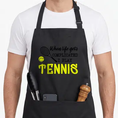 Tablier de cuisine noir avec une raquette de tennis et le texte When life gets complicated I play Tennis en jaune et noir.