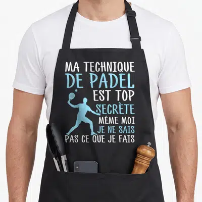 Tablier de cuisine noir avec silhouette bleue d'un joueur de padel et texte blanc et bleu humoristique sur la technique secrète.