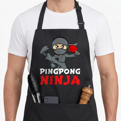 Tablier de cuisine noir avec un ninja gris tenant une raquette de ping-pong rouge et le texte Pingpong Ninja.