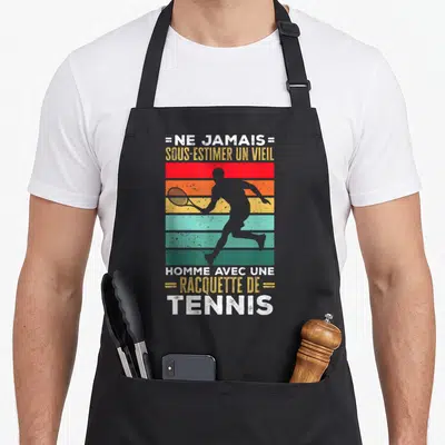 Tablier de cuisine noir avec silhouette de joueur de tennis sur bandes colorées et texte humoristique en style rétro.