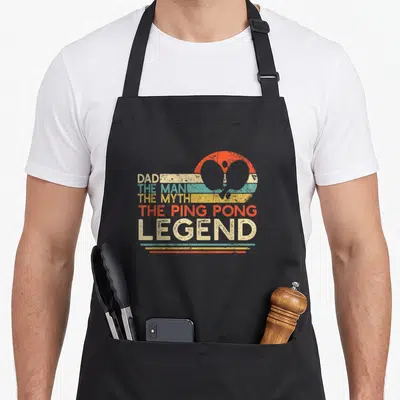 Tablier de cuisine noir avec illustration vintage Dad The Man The Myth The Ping Pong Legend et raquettes stylisées.