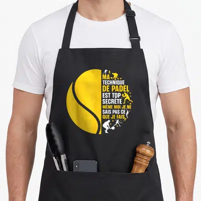 Tablier de cuisine noir avec motif balle de padel jaune et silhouettes de joueurs en action sur fond blanc et orange.