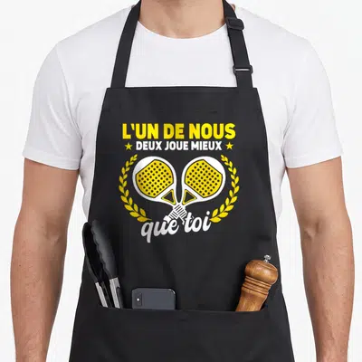 Tablier de cuisine noir avec deux raques de padel jaunes croisées et une inscription humoristique en blanc et jaune.
