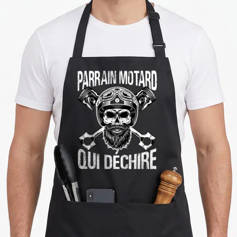Tablier de cuisine noir avec une tête de mort tatouée à casque et pistons croisés.