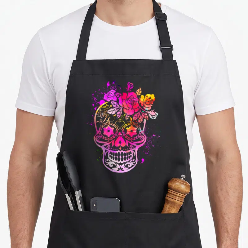Tablier de cuisine noir avec un crâne sucré rose orné de roses et de motifs floraux colorés.