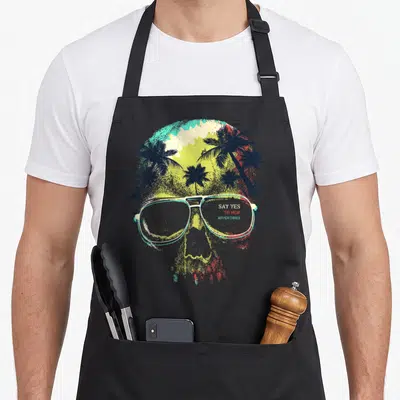Tablier de cuisine noir avec un crâneSugar Skull portant des lunettes aviateurs sur fond de palmiers colorés.