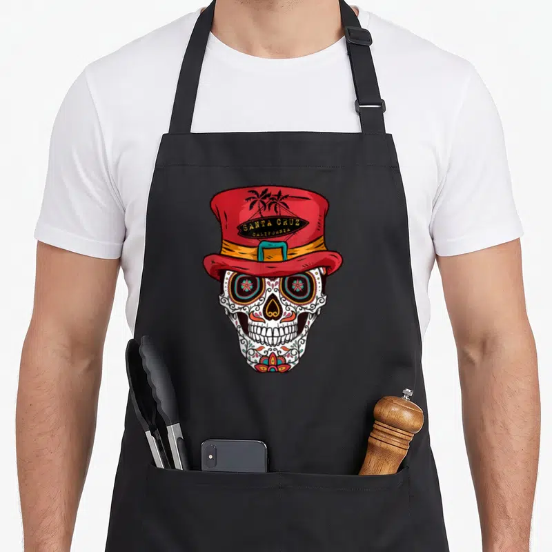 Tablier de cuisine noir orné d'un crâne stylisé Day of the Dead portant un chapeau haut de forme rouge Santa Cruz California.