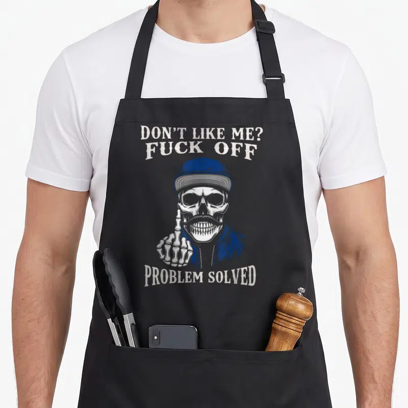 Tablier de cuisine noir avec crâne vintage en casquette bleue levant le majeur et texte provocateur imprimé en blanc.