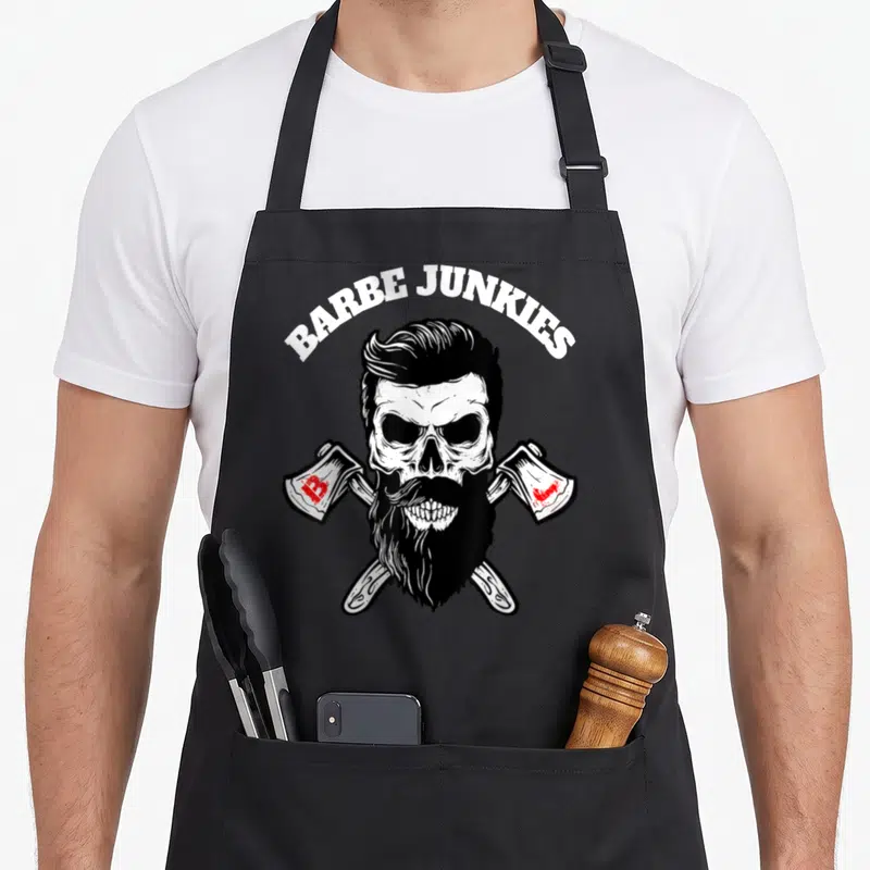 Tablier de cuisine noir avec un crâne barbu aux haches croisées et l'inscription Barbe Junkies en haut.