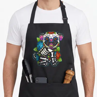 Tablier de cuisine noir avec un chiot squelette calavera mexicain entouré de roses colorées et de motifs floraux.