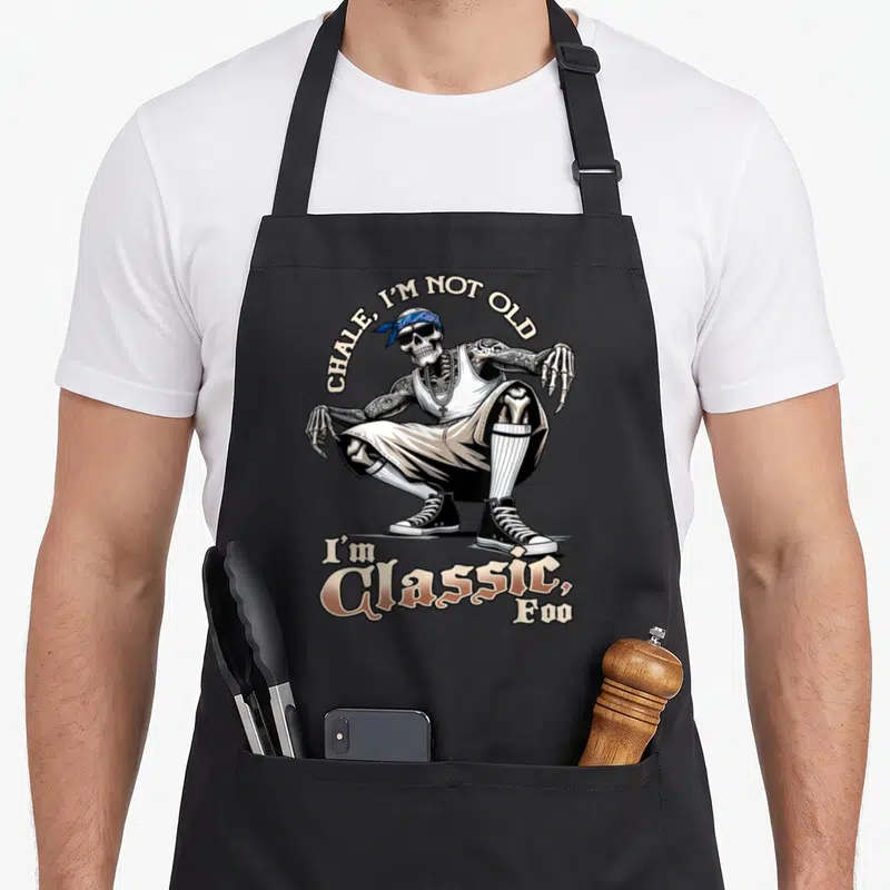 Tablier de cuisine noir avec squelette cholo en tenue urbaine et texte humoristique imprimé.