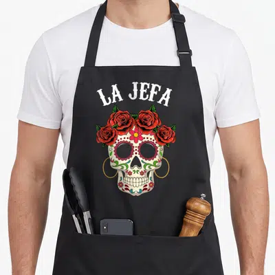 Tablier de cuisine noir avec crâne sugar skull La Jefa orné de roses rouges et fleurs colorées.