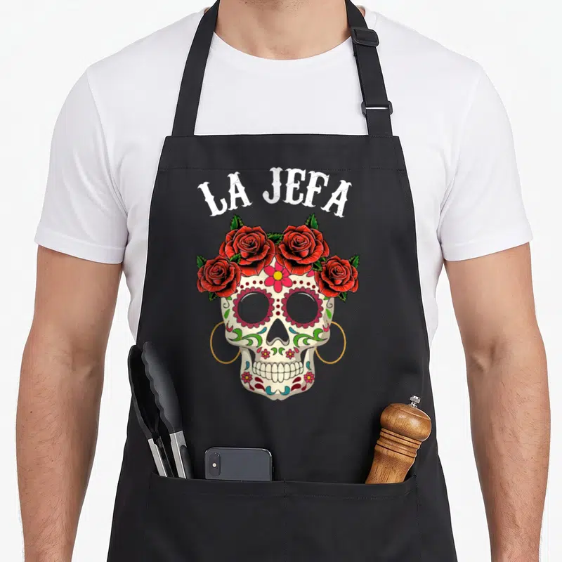 Tablier de cuisine noir avec crâne sugar skull La Jefa orné de roses rouges et fleurs colorées.