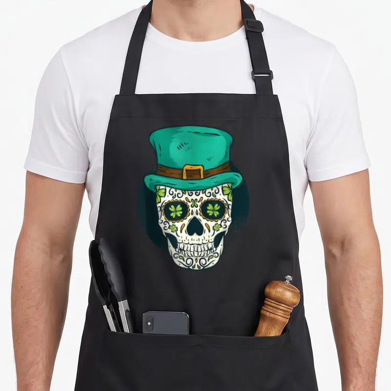 Tablier de cuisine noir avec un crâne décoré de trèfles verts portant un chapeau haut de forme turquoise.