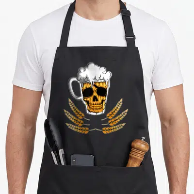 Tablier de cuisine noir avec illustration d'un crâne doré en forme de verre de bière surmonté de mousse et entouré d'épis de wheat.