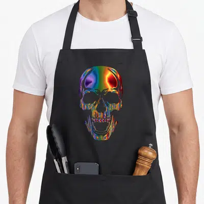 Tablier de cuisine noir avec une tête de mort en métal chromé arc-en-ciel brillant au centre.