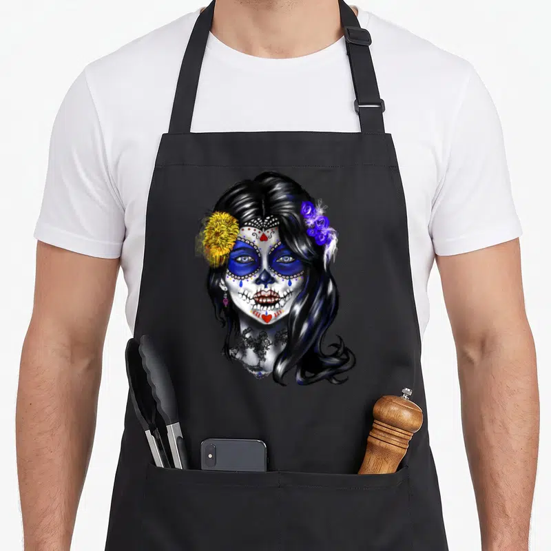 Tablier de cuisine noir avec illustration crâne femme Dia des morts fleurs jaunes roses bleues et larmes stylisées.