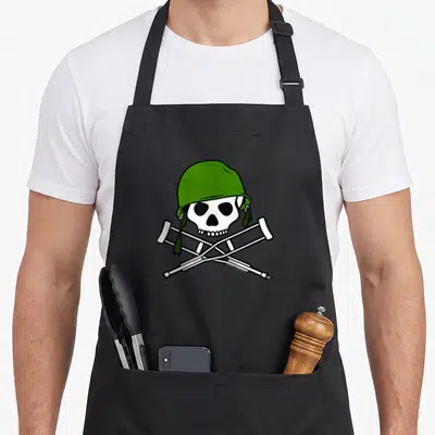 Tablier de cuisine noir avec un crâne portant un casque vert au-dessus de deux béquilles blanches croisées.