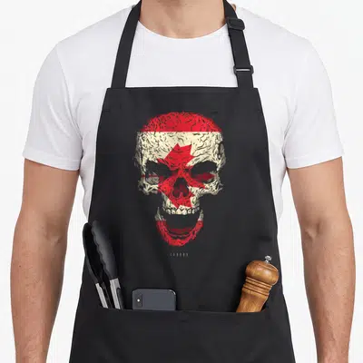 Tablier de cuisine noir avec un crâne beige et rouge intégrant le drapeau canadien et la feuille d'érable au centre.