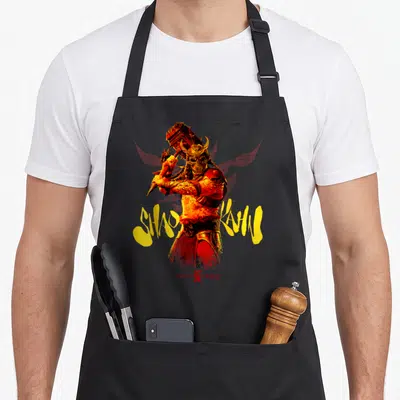 Tablier de cuisine noir avec illustration de Shao Kahn tenant un marteau et le logo Mortal Kombat en bas.