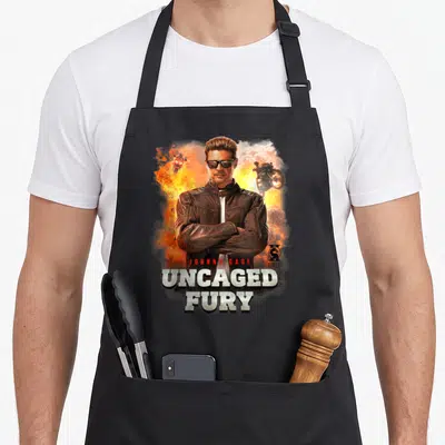 Tablier de cuisine noir avec une illustration de Johnny Cage et le texte Uncaged Fury sur fond d'explosion.
