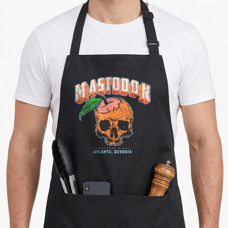 Tablier de cuisine noir avec illustration d'un crâne orange en forme de pêche et du texte Mastodon Atlanta Georgia en lettres rétro.