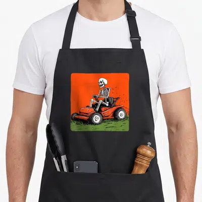 Tablier de cuisine noir avec illustration d'un squelette conduisant une tondeuse à gazon sur fond orange vif.