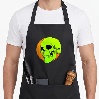Tablier de cuisine noir avec illustration d'un crâne vert fluorescent sur cercle orange, style graffiti rétro.