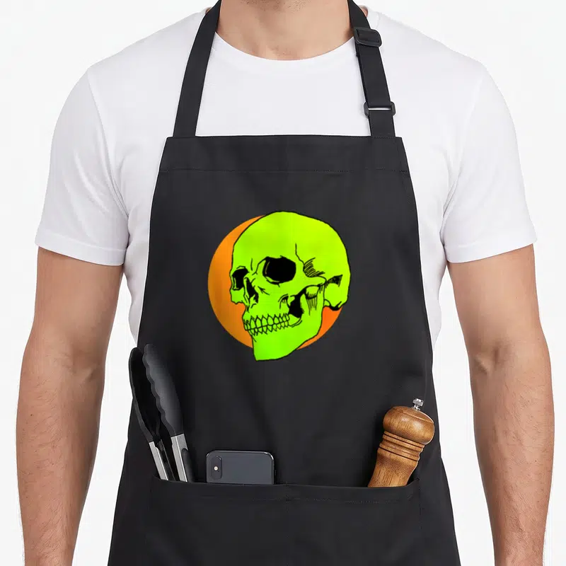 Tablier de cuisine noir avec illustration d'un crâne vert fluorescent sur cercle orange, style graffiti rétro.