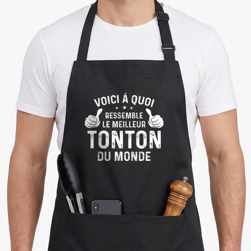 Tablier de cuisine noir avec inscription Voici à quoi ressemble le meilleur tonton du monde et deux pouces levés blancs.