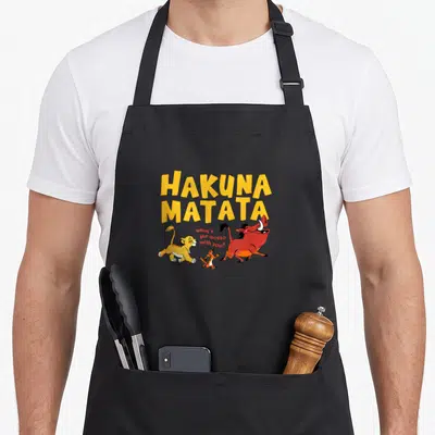 Tablier de cuisine noir avec inscription Hakuna Matata jaune et illustration de Simba, Timon et Pumbaa courant ensemble.