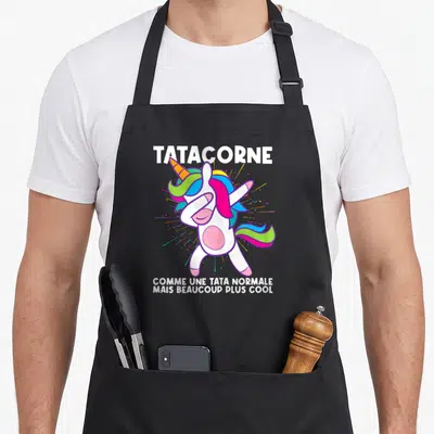 Tablier de cuisine noir avec illustration licorne colorée en pose dab et texte blanc Tatacorne comme une tata normale mais beaucoup plus cool.