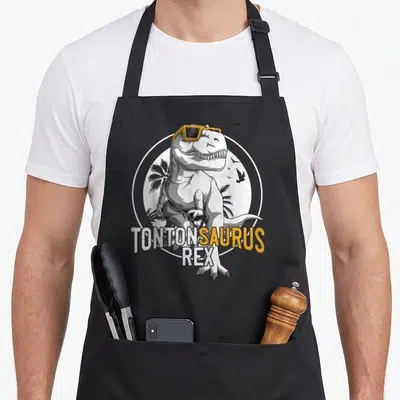 Tablier de cuisine noir avec illustration dinosaure aux lunettes jaunes et texte Tontonsaurus Rex.