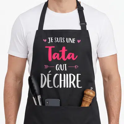 Tablier de cuisine noir avec l'inscription Je Suis Une Tata Qui Déchire en blanc et rose, orné de cœurs et d'une flèche.