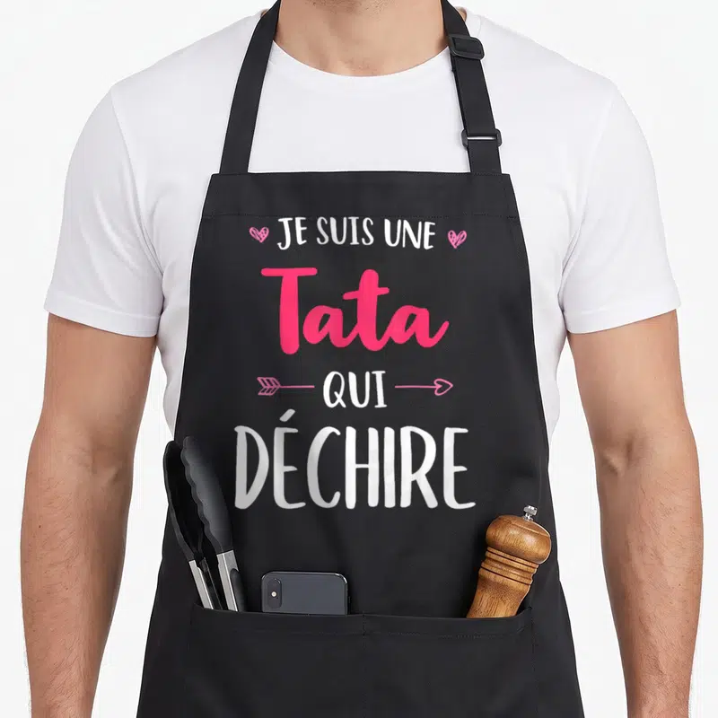 Tablier de cuisine noir avec l'inscription Je Suis Une Tata Qui Déchire en blanc et rose, orné de cœurs et d'une flèche.