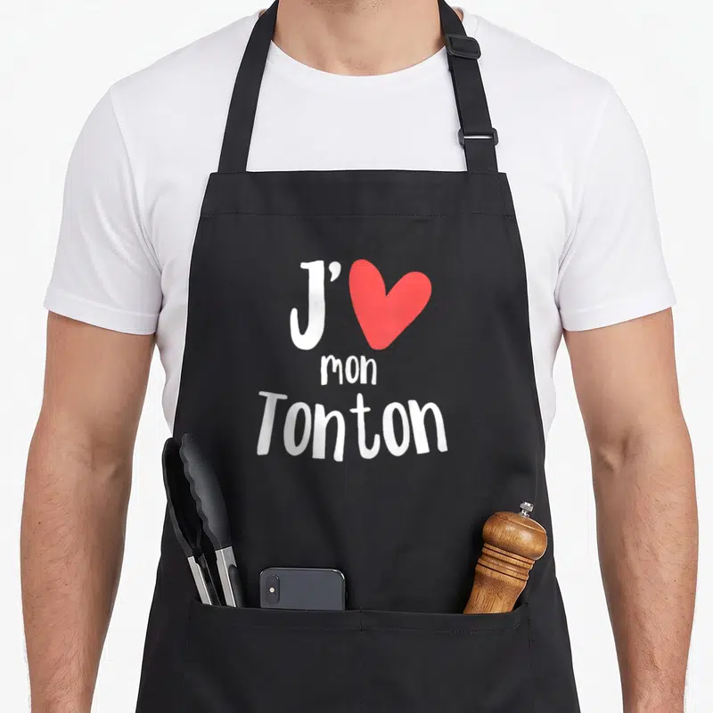 Tablier de cuisine noir avec l'inscription J'aime mon Tonton et un cœur rouge stylisé au centre du torse.