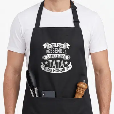 Tablier de cuisine noir avec inscription Voici à quoi ressemble la meilleure tata du monde et deux pouces levés.