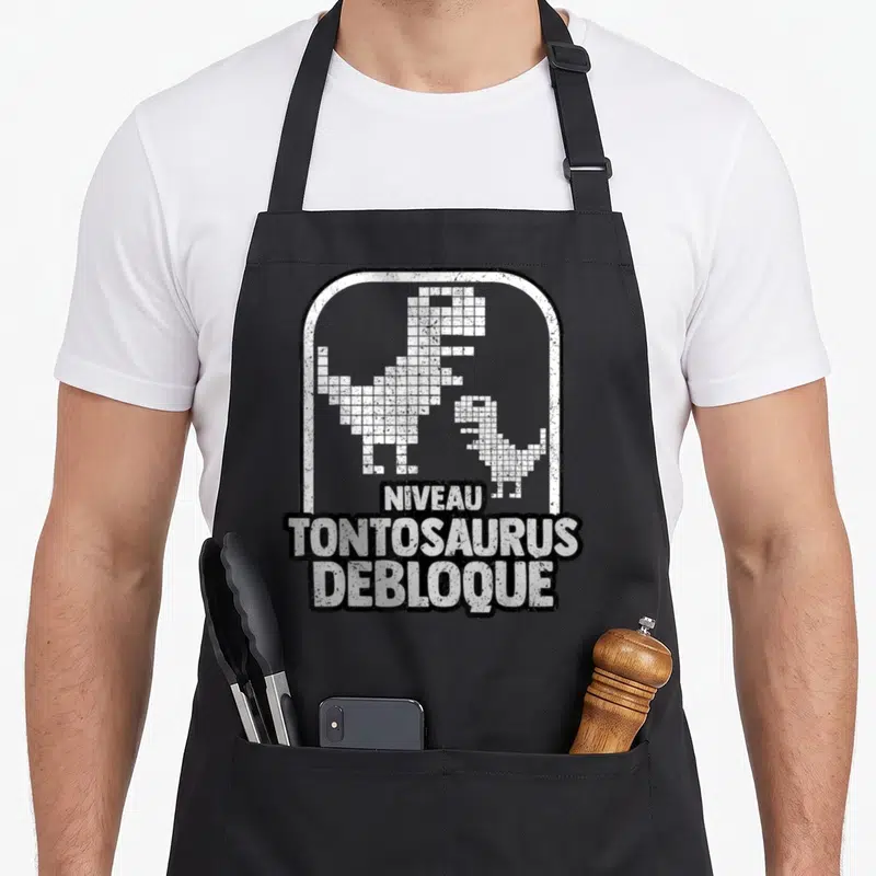 Tablier de cuisine noir avec inscription Niveau Tontosaurus debloque et deux dinosaures en pixels blancs.