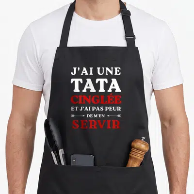 Tablier de cuisine noir avec l'inscription J'ai une tata cinglée et j'ai pas peur de m'en servir en blanc et rouge.