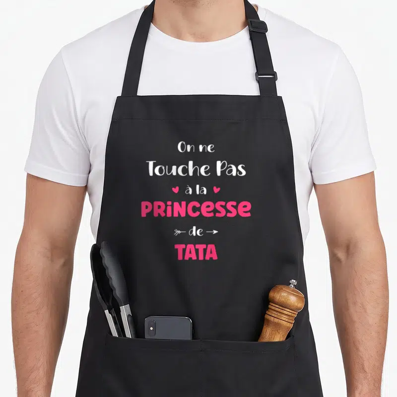 Tablier de cuisine noir avec inscription blanche et rose On ne Touche Pas à la Princesse de Tata accompagnée de cœurs et flèches.