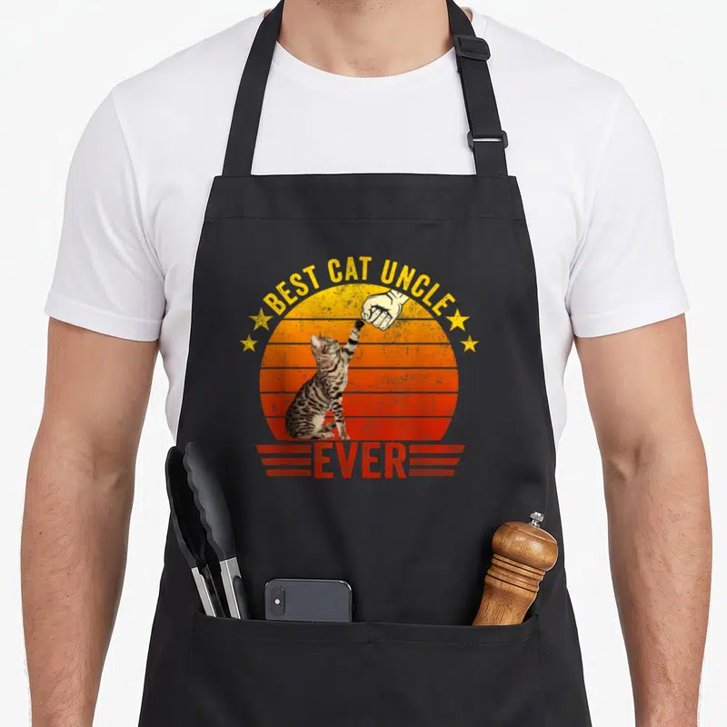 Tablier de cuisine noir avec illustration d'un chat effectuant une poignée de main sur fond de soleil orange vintage.