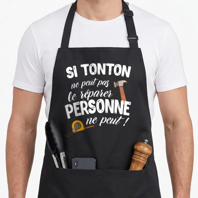 Tablier de cuisine noir avec inscription blanche et illustrations d'un marteau et d'un mètre ruban jaune.