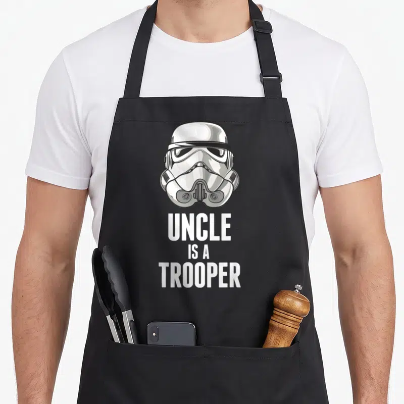 Tablier de cuisine noir avec illustration de casque de Stormtrooper et texte blanc en dessous.