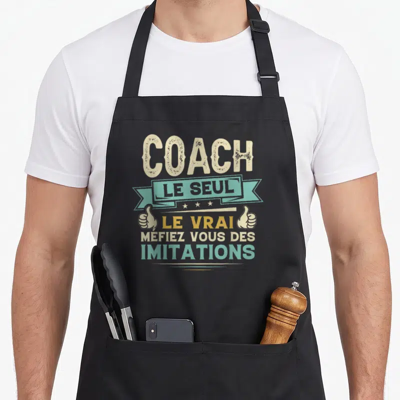 Tablier de cuisine noir avec inscription Coach Le Seul Le Vrai Mefiez Vous Des Imitations et deux mains en signe d'approbation.