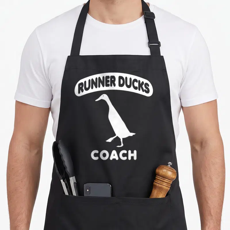 Tablier de cuisine noir avec silhouette blanche d'un canard et les mots Runner Ducks Coach imprimés.
